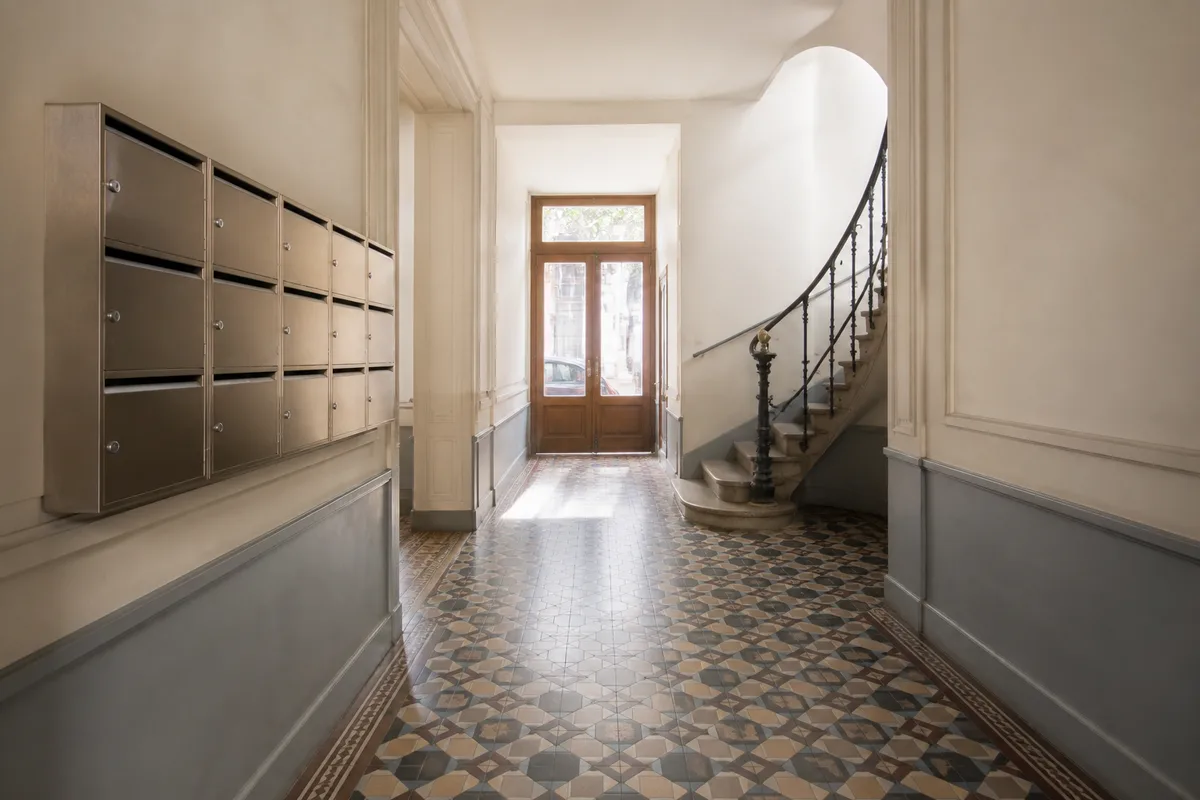 Hall d&rsquo;immeuble collectif ancien avec boîtes aux lettres et escalier en pierre